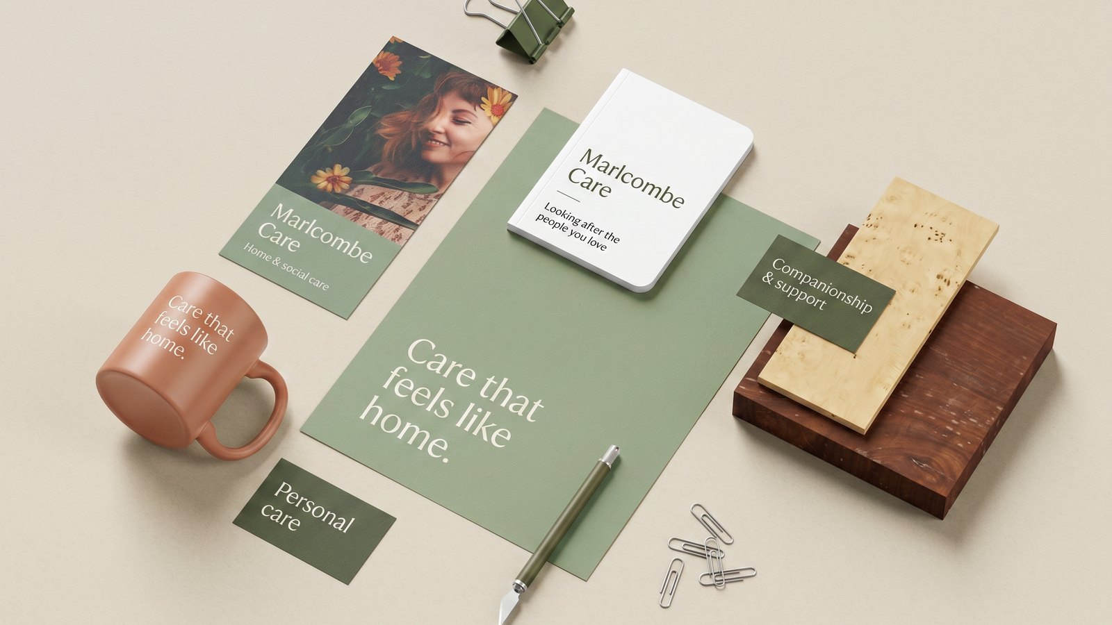 Branded stationery flat-lay for an example care company — business cards, a brochure and a mug in warm sage and clay tones